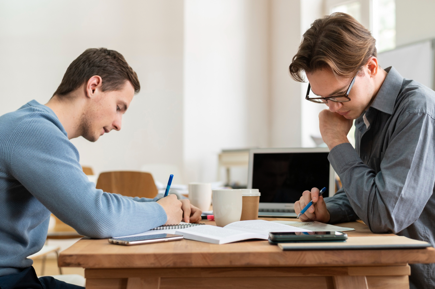 Deux étudiants concentrés révisent ensemble chez occi fomation dans le tarn avec carnets, café et ordinateur